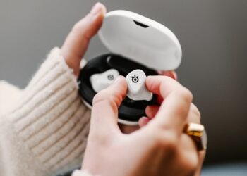 SteelSeries Arctis GameBuds in white with a lady's hand removing one bud from the box