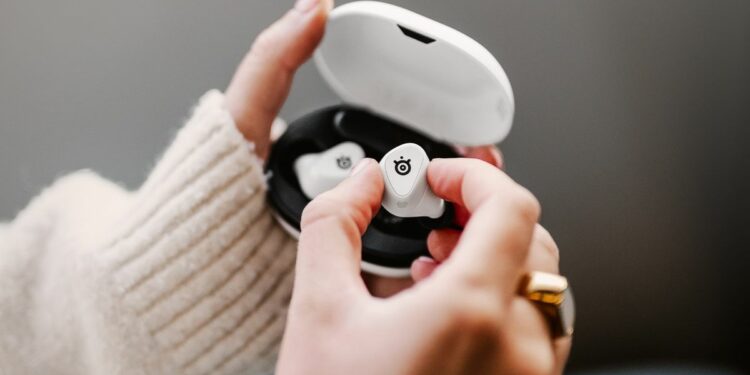 SteelSeries Arctis GameBuds in white with a lady's hand removing one bud from the box